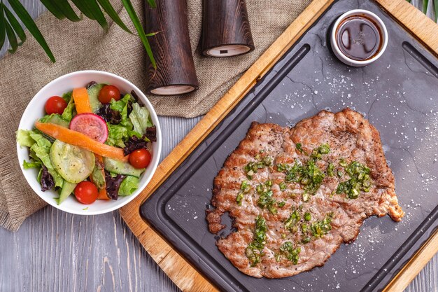 Top view grilled chop meat with vegetable salad and sauce on blackboard
