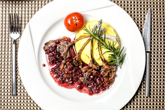 Top view grilled lamb ribs in pomegranate sauce with mashed potatoes tomato and rosemary