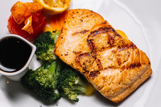 Top view grilled red fish steak with broccoli a slice of lemon tomato and narsharab sauce