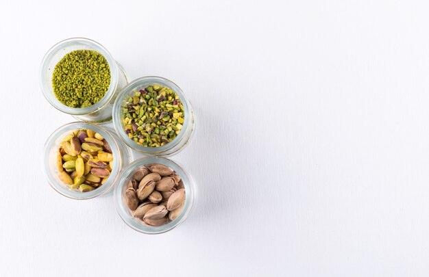 Top view ground, milled, crushed or granulated pistachios in glass jars on white 