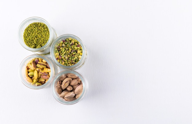 Top view ground, milled, crushed or granulated pistachios in glass jars on white 