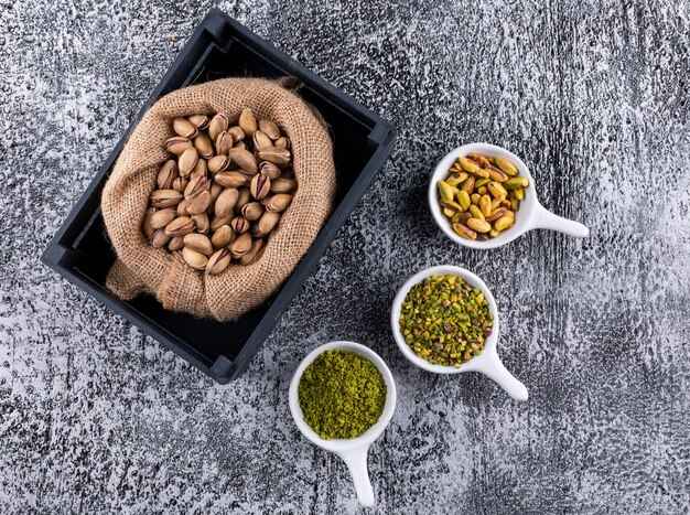 Top view ground, milled, crushed or granulated pistachios in sack on gray texture background horizontal