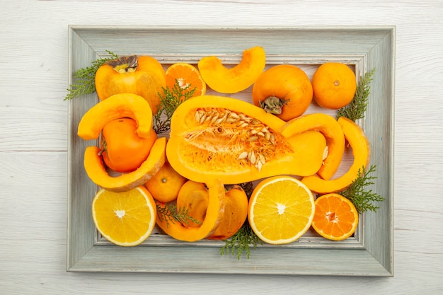 Free photo top view half butternut squash cut orange persimmons mandarins on frame on white table