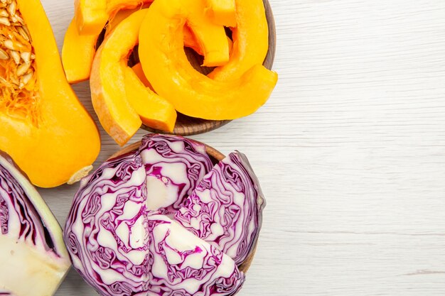 Top view half butternut squash half red cabbage squash and red cabbage slices in bowls on grey table with free place