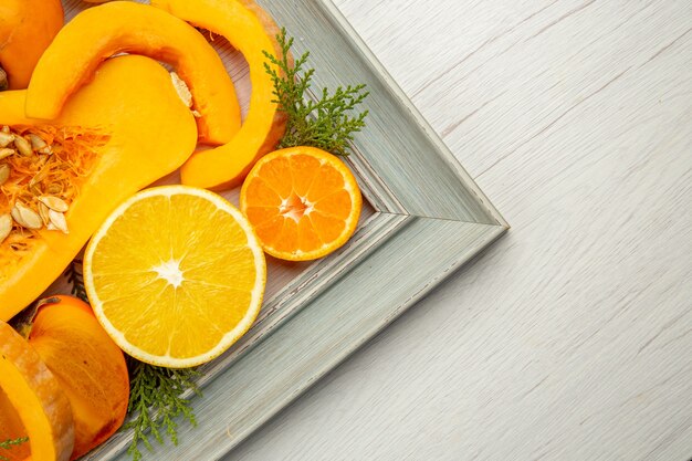 Top view half butternut squash persimmons mandarins half orange on grey frame on white table