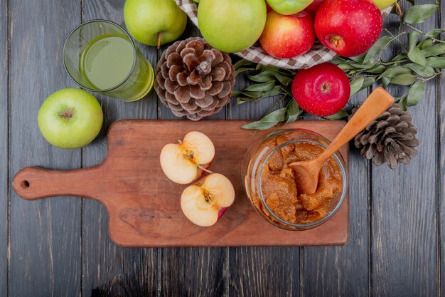 top view of - and half cut apple on cutting board with apple juice basket of apples pinecone and leaves on wooden table