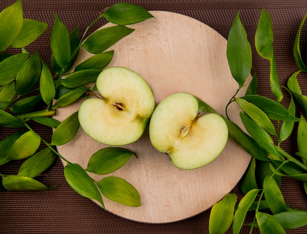 Top view of half cut apple with leaves on cutting board and on cloth surface