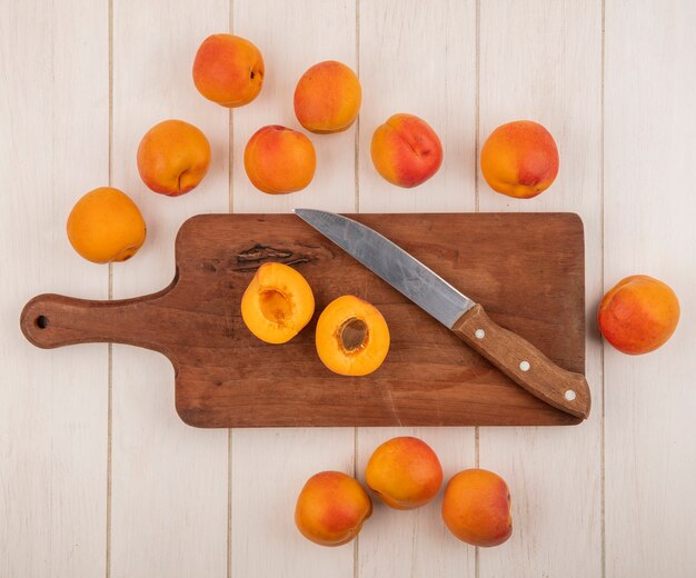 Вид сверху на половину абрикоса с ножом на разделочной доске и узор абрикосов на деревянном фоне