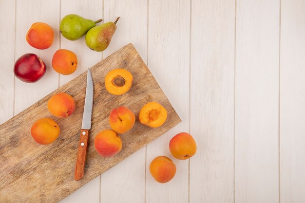 Top view of half cut and whole apricots and knife on cutting board with pattern of fruits as peach apricot and pear on wooden background with copy space