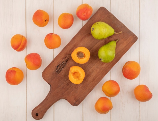 Top view of half cut and whole fruits as apricot and pears on cutting board and pattern of apricots on wooden background
