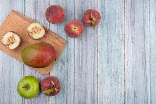 灰色の木製の表面にマンゴーアップルと木製キッチンボード上の半分の桃のトップビュー