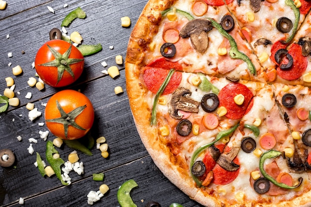 Вид сверху на половину пиццы пепперони, расположенной рядом с томатным сыром, кукурузой и болгарским перцем
