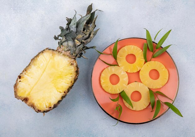 Top view of half of pineapple with pineapple slices in plate on white surface