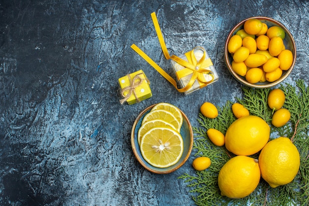 Top view of half and whole fresh citrus fruits and yellow gift boxes on dark background