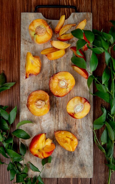 Top view of halves of fresh ripe peaches on a wooden cutting board with green leaves on rustic table