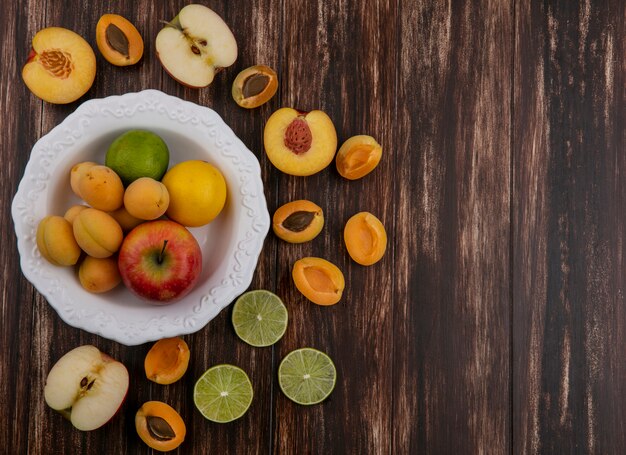 Top view of halves of a mix of fruits apricots apples peach and lime on a wooden surface