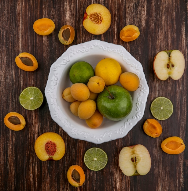 Free photo top view of halves of a mix of fruits apricots apples peach and lime on a wooden surface