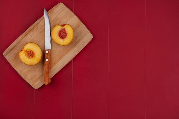 Вид сверху половинки персика с ножом на доске на красной поверхности