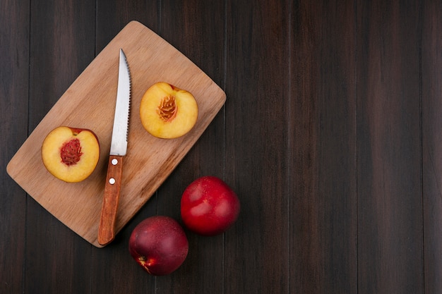 Top view of halves of peaches on a blackboard with a knife on a wooden surface