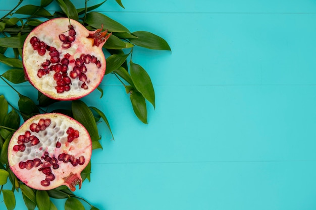 Free photo top view of halves of pomegranate on leaf branches on a blue surface