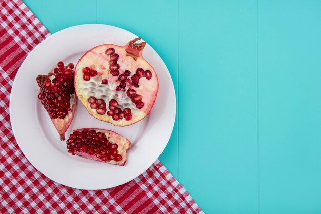 Top view of halves of pomegranate on a plate with a checkered red towel on a blue surface