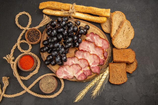 Foto gratuita fette di prosciutto vista dall'alto con condimenti all'uva e fette di pane su sfondo scuro