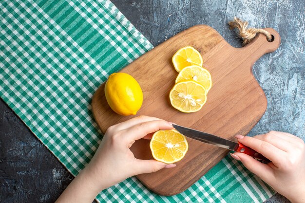 Top view of a hand chopping fresh lemons on a wooden cutting board on dark background