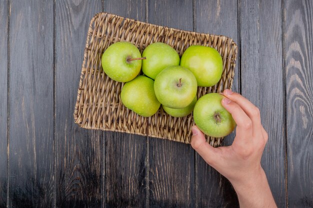 나무 테이블에 바구니 접시에 사과 녹색 사과 들고 손의 상위 뷰