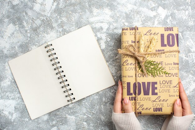 Top view of hand holding big packed gift for Christmas and open notebook on ice surface