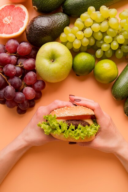 Top view hand holding burger near fruits