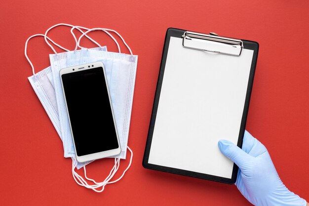 Top view of hand holding clipboard with medical masks and smartphone