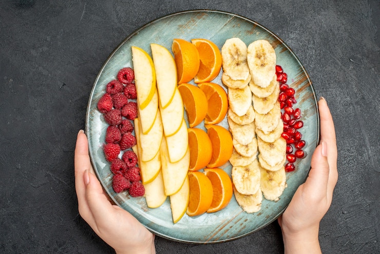 Free Photo top view of hand holding collection of chopped fresh fruits on a blue plate on black table