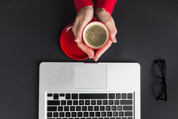 ノートパソコンを机の上のコーヒーカップを持っている手の平面図