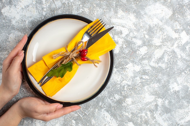 Top view of hand holding cutlery set for meal on a white plate on the right side on ice surface