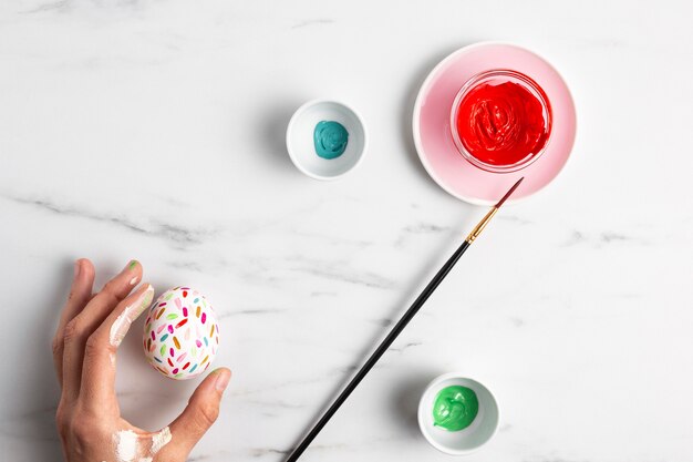 Top view of hand holding decorated easter egg with paint and paintbrush