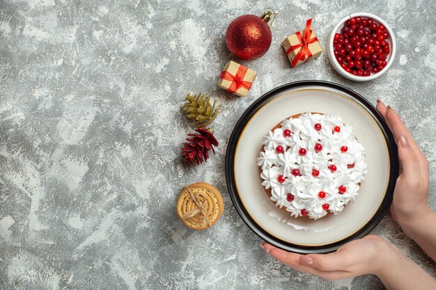 Top view of hand holding delicious cake with cream currant on a plate and gift boxes