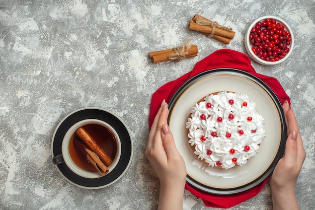 Top view of hand holding delicious creamy cake decorated with fruits on a red towel