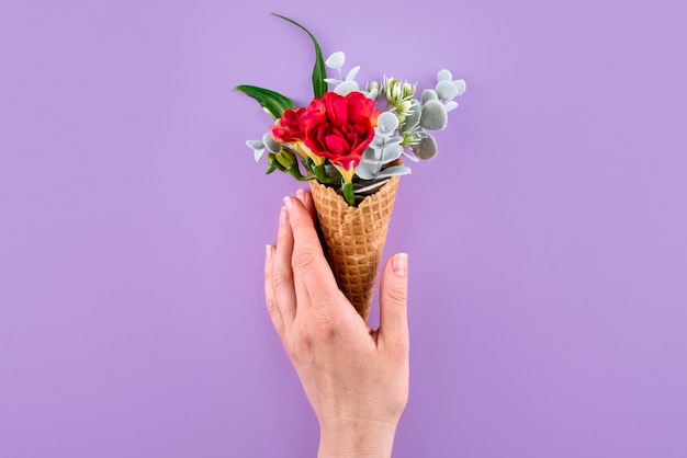 Free photo top view hand holding eco ice cream cone with flowers