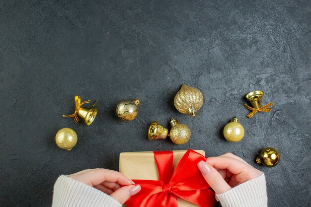 Top view of hand holding a gift box with red ribbon and decoration accessories on dark table