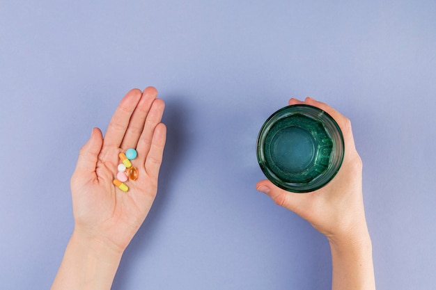 Free photo top view hand holding medicine and glass with water