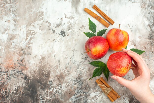 混合色の背景の左側に新鮮な天然の赤いリンゴとシナモンライムの1つを持っている手の上面図