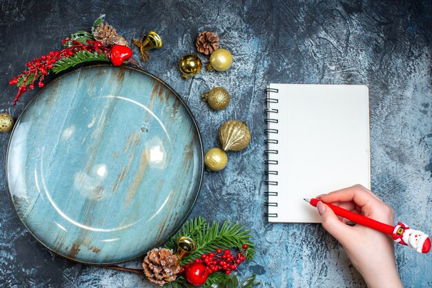 Top view of hand holding a pen on spiral notebook and empty blue plate on dark background