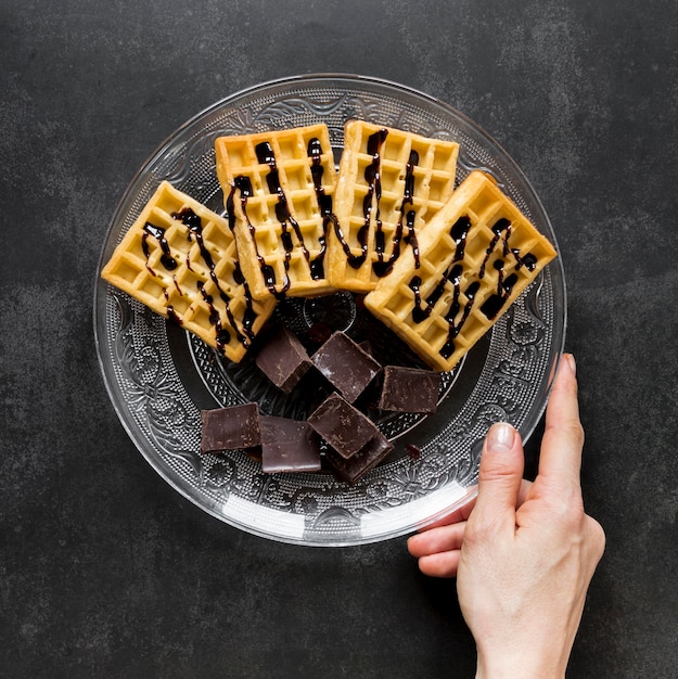 Top view of hand holding plate with waffles and chocolate pieces