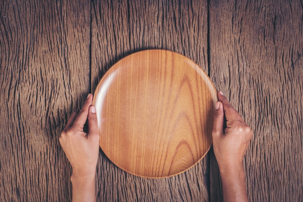 Top view hand holding plate on wood background