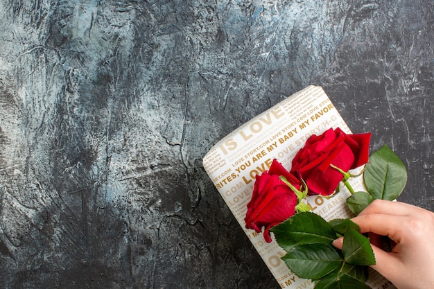 Top view of hand holding red roses on beautiful gift box on icy dark background with free space