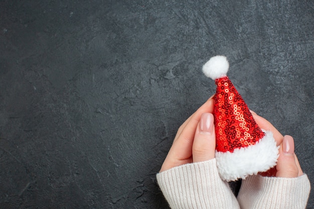 Free photo top view of hand holding santa claus hat on the left side on dark background