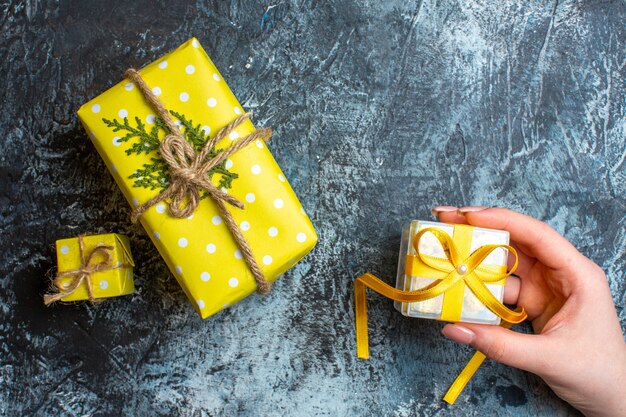 어두운 배경에 작은 선물 상자와 다른 두 개의 크리스마스 선물 상자를 들고 있는 손의 상위 뷰