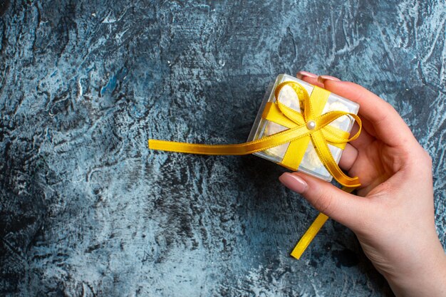 Top view of hand holding a small gift box on the right side on dark background