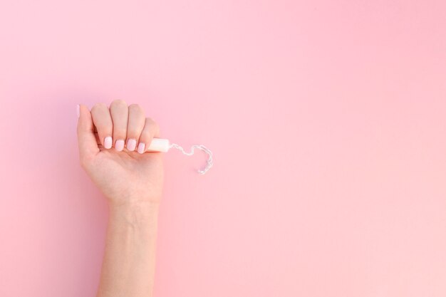 Top view hand holding tampon on pink background