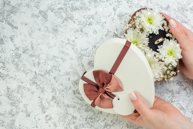 Top view of hand opening heart shaped box with beautiful flowers and ring on the left side on ice background